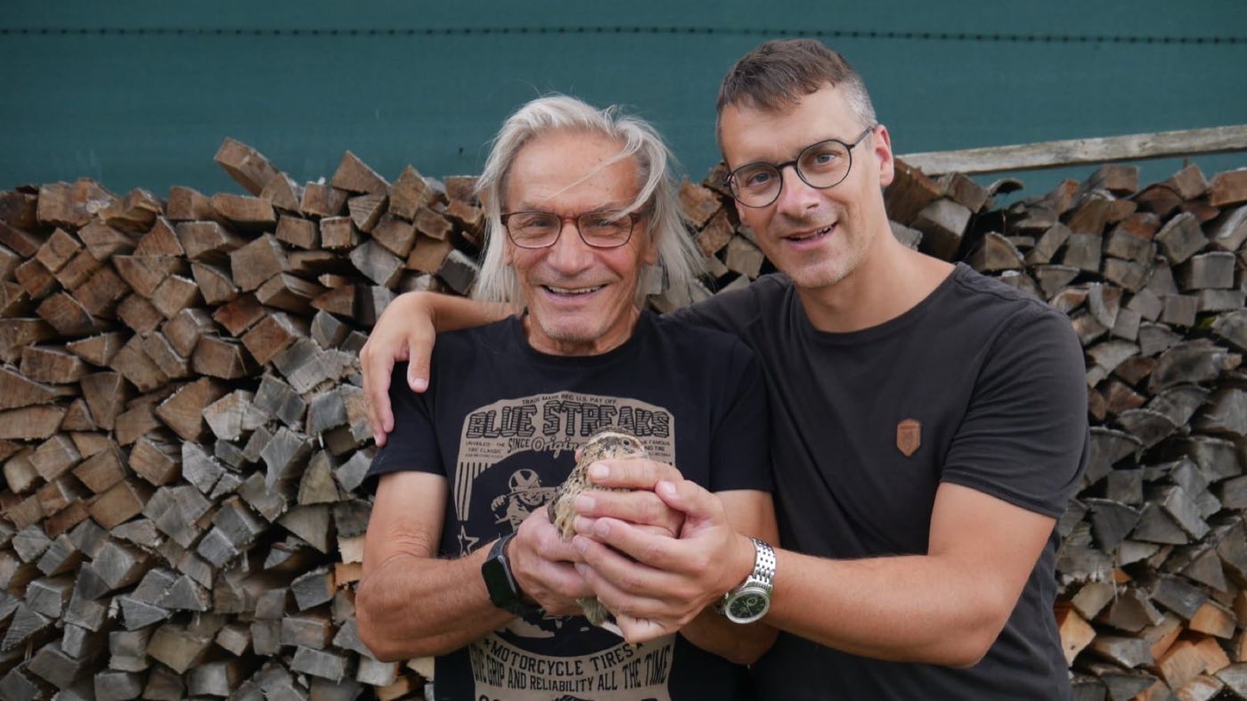 Franz und David Ertler vor dem Holzstoß, mit einer Wachtel in den Händen