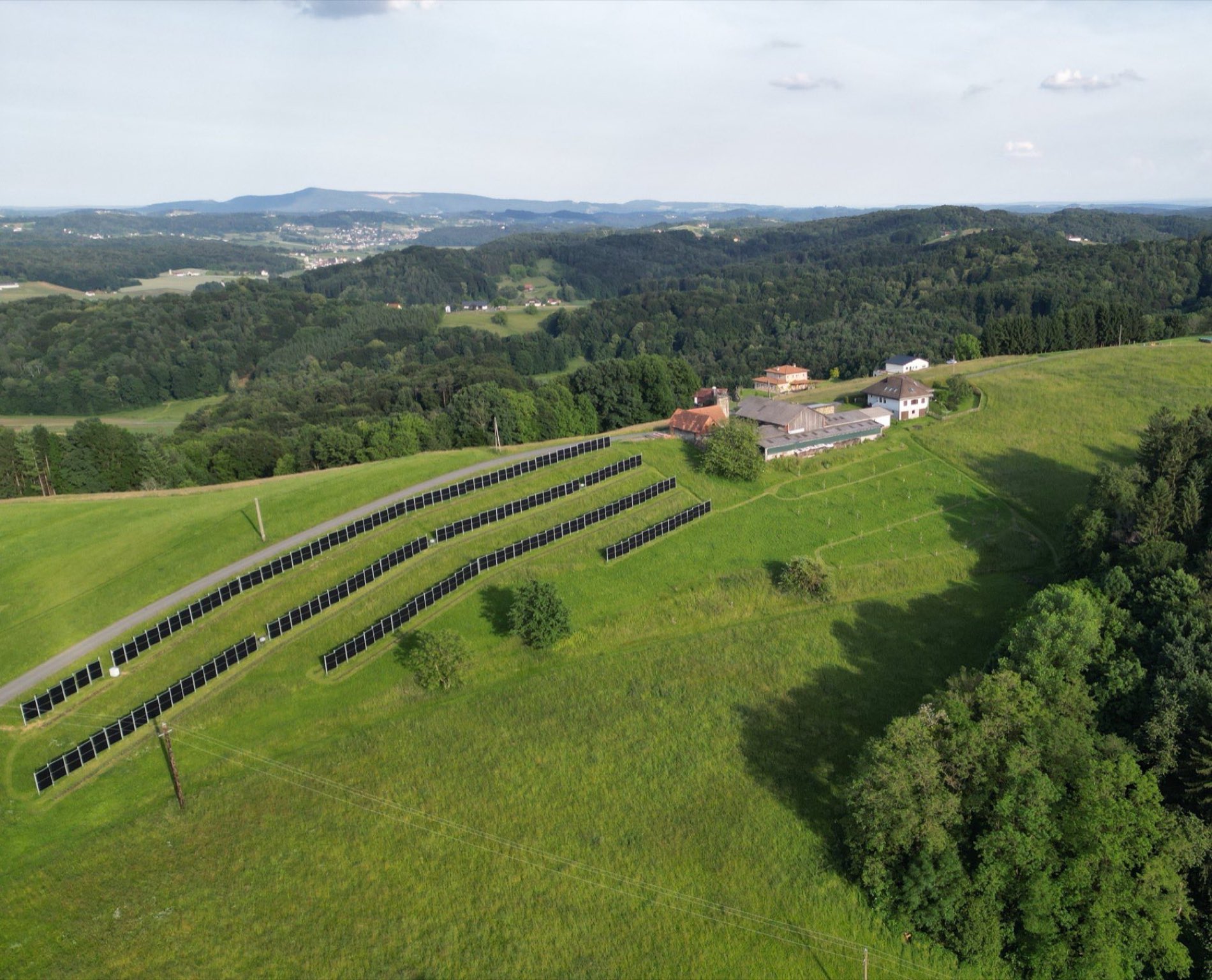 Luftaufnahme des Ertler Hofs mit Wiesen, Wald und Photovoltaikreihen