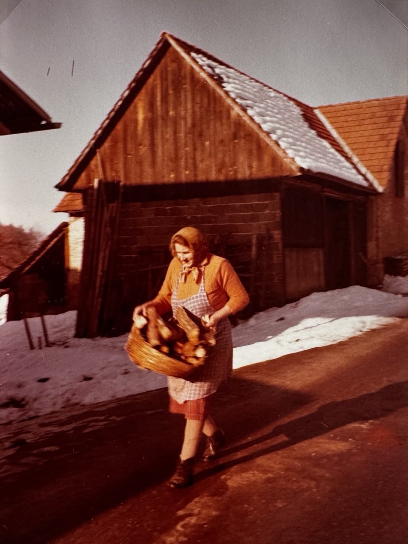Ältere Farbaufnahme: Arbeit am Ertler Hof im Winter mit einem Korb voll Holz
